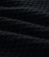 Buzo de punto negro con textura geométrica tipo colmena, cuello alto y mangas largas con puños ajustados.