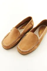 Mocasines de cuero vacuno color beige con acabado mate, costuras visibles artesanales en el empeine y suela de perfil bajo.