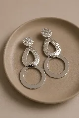 Aros colgantes dorados compuestos por un disco superior texturizado, una pieza central en forma de gota con textura martillada y un aro circular liso en la parte inferior.
