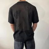 Camisa de tejido de punto calado color negro, con cuello solapa, cierre frontal de botones y mangas cortas.