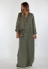 Vestido largo tipo camisero de color verde oliva, con cuello clásico, cierre frontal completo con botones y mangas largas con opción de arremangar. Presenta un corte holgado y fluido.