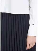 Camisa blanca de algodón orgánico, nailon y elastano, con cuello de rayas celestes y cierre con botones dorados. Tiene corte boxy, manga larga, bolsillo de parche en el pecho y logo de Tommy Hilfiger bordado en el puño.