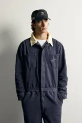 Mono oversize fit de algodón con estructura espiga en color azul marino, con cuello solapa en contraste de color tostado, manga larga, bolsillos de plastrón en el pecho con firma bordada, trabillas laterales en la cintura y cierre frontal con cremallera y botonadura oculta.