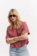 Camisa de manga corta color rosado, con cuello camisero, bolsillos frontales con solapa, botones a tono y diseño ligeramente recortado.