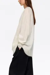 Cardigan largo de corte oversize, color blanco, con escote en pico, cierre frontal de botones y bolsillos de plastrón. Presenta mangas largas con puños acanalados.