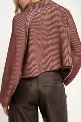 Sweater de punto acanalado color camel, con cuello alto y cierre frontal parcial. Presenta mangas largas con costuras raglán y un corte ligeramente cropped.