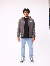 Canguro gris con capucha, cierre frontal completo y bolsillos tipo canguro. Presenta detalles de líneas blancas en las mangas y estampados gráficos en el pecho.