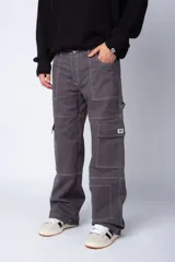 Pantalón tipo carpintero de corte relaxed fit y tiro medio, confeccionado en denim negro con costuras a contracolor en blanco. Presenta múltiples bolsillos cargo laterales, un bolsillo con cierre en la parte inferior y presillas utilitarias.