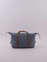 Bolso de viaje tipo duffle, confeccionado en cuero natural color azul con textura, con detalles de correas y asas en cuero color suela. Cuenta con cierre superior, bolsillo interior con cierre y compartimento para celular.