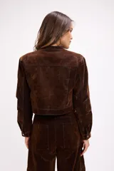 Chaqueta corta de terciopelo negro con efecto desgastado en tono azulado, cuello mao, cierre frontal metálico y bolsillos frontales con tapa y botón.