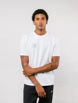 Remera de manga corta color blanco con cuello redondo. Presenta un pequeño logo circular de Umbro estampado en el pecho con la leyenda 'Born to Play'.