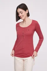 Remera blanca de manga larga, entallada, con cuello redondo y una hilera de botones en el frente. Incluye un pequeño bolsillo decorativo en el pecho.