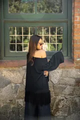 Buzo de punto color negro, con diseño oversize, cuello redondo y mangas largas. Presenta un detalle de flecos en el ruedo inferior que aporta movimiento a la prenda.