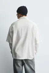 Camisa de corte relajado confeccionada en tejido fluido con mezcla de viscosa, color negro. Presenta cuello solapa, manga corta, cierre frontal con botones y un bordado a contraste en el pecho.