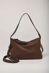 Cartera de hombro confeccionada en gamuza color chocolate, con cierre superior y doble sistema de correas: una fija de cuero liso negro para llevar al hombro y una correa larga ajustable y extraíble de gamuza y cuero negro para usar cruzada.