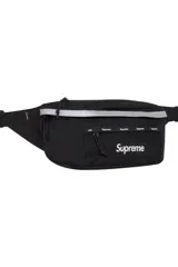 Riñonera Supreme color negro, con bolsillo frontal de malla, detalle reflectante en la parte superior y logo de la marca estampado en el frente.