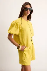 Blusa de lino color amarillo, con cuello redondo, mangas cortas abullonadas y cierre frontal con botones.