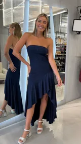 Vestido largo azul marino con acabado brillante, diseño strapless y corte asimétrico con volados en la falda.