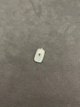 Dije de piedra natural con forma rectangular y bordes redondeados, con detalle central de engaste metálico dorado y piedra pequeña incrustada. Disponible en tres variantes de color: rojo, blanco traslúcido y marrón.