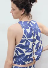 Top crop sin mangas con cuello redondo y cierre de botones en la parte posterior. Presenta un diseño recto con tirantes anchos y un estampado floral en tonos azul y blanco.