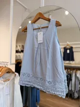 Blusa sin mangas de color beige, confeccionada en mezcla de lyocell y lino, con diseño de pliegues en el frente y detalle de encaje tipo puntilla en el ruedo.