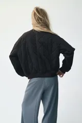 Campera bomber negra, acolchada con patrón de rombos. Presenta cuello, puños y bajo acanalados. Tiene cierre frontal con botones a presión y dos bolsillos de parche en la parte delantera.