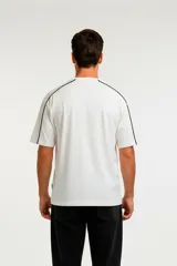 Remera de algodón de corte holgado, color blanco con detalle de líneas negras en los hombros y mangas.