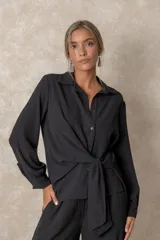 Camisa de corte clásico con cuello camisero, mangas largas con puños abotonados y cierre frontal con botones. Presenta un diseño con lazo ajustable integrado en la cintura que permite entallar la prenda.