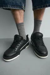 Zapatilla deportiva de estilo urbano con cordones, confeccionada en una combinación de piezas de cuero sintético. Presenta un diseño con detalles en contraste, suela con volumen bicolor y tirador en el talón.