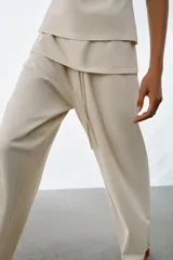 Pantalón de algodón compacto color beige, de tiro alto con cintura elástica y detalle de fajín y cordones.