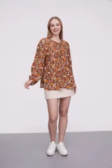 Blusa marrón con estampado de flores color naranja y blanco, con cuello redondo con abertura y mangas largas abullonadas.