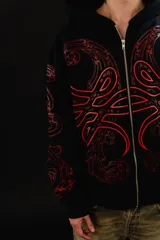 Hoodie con cierre frontal completo, confeccionado en algodón de tejido grueso. Presenta un diseño estampado en serigrafía con motivos de hojas de acanto en color rojo sobre fondo negro. Cuenta con bolsillos laterales y cierre metálico YKK.