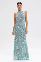 Vestido largo de fiesta color verde agua, confeccionado en tul con bordado artesanal de mariposas y motivos geométricos. Presenta escote halter alto, detalles de flecos integrados al bordado y transparencias sofisticadas.