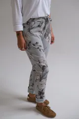 Pantalón de corte recto con cintura elástica y cordón ajustable, confeccionado en tela con estampado floral en tonos grises y blancos sobre base celeste.