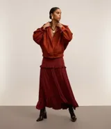 Falda midi evasé color borgoña de poliéster satinado, con cierre trasero invisible, volado en la cadera y ruedo fruncido.