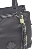 Cartera tipo bolso de mano color negro, confeccionada en material textil. Cuenta con doble asa superior, correa ajustable extraíble, detalle de dije colgante con cordones en tonos verde lima y negro, y logo circular grabado en el frente.