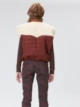 Chaleco de corte cuadrado con diseño bicolor en tonos terracota y crema. Presenta cierre frontal metalizado, parches de nylon en el pecho, interior forrado en corderito y cordón ajustable en el ruedo.