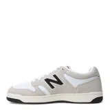 Championes urbanos New Balance modelo 480 Court, con diseño de inspiración retro. Presentan una combinación de cuero blanco perforado en la puntera y paneles laterales con superposiciones de gamuza en tono gris claro. Incluyen el logo 'N' característico en color negro en los laterales, cordones blancos y una suela de goma con base negra.