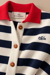 Cárdigan de punto a rayas horizontales blancas y azul marino, con cuello tipo polo en color rojo, cierre frontal de botones y puños rojos. Presenta un pequeño bordado decorativo en el pecho.
