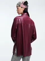 Camisa de corte oversize confeccionada en tejido jersey con acabado brillante. Presenta cuello en punta, cierre frontal con botones, mangas largas con puños anchos y tajos laterales en el ruedo.