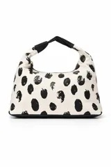 Cartera tipo hobo bag de tela color crema con estampado de manchas negras irregulares. Tiene un asa de hombro de cuero sintético negro y cierre de cremallera.