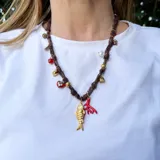 Collar corto hecho con cinta de tela blanca y dijes dorados, rojos y nacarados con forma de pez, corazón, coral, flor y cuentas.