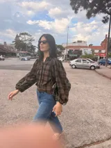 Camisa de corte oversize con estampado de cuadros escoceses en tonos negro y marrón. Presenta cuello camisero, cierre frontal con botones y mangas largas con volumen y puños elásticos.