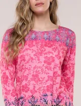 Remera evasé de manga tres cuartos y escote bote, confeccionada en rayón elastizado de color rosado con textura flameada y estampado floral en tonos fucsia y azul.
