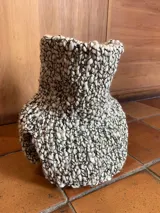 Cuello tejido a mano en lana merino color crudo, con textura acanalada y aberturas laterales.