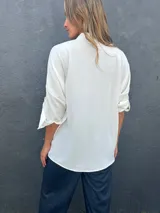 Camisa blanca de corte holgado y asimétrico, con cuello camisero y cierre frontal de botones.