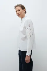 Camisa blanca de manga larga con cuello alto fruncido y bordados calados en el pecho y los hombros.