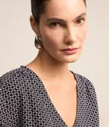 Blusa de crepé con estampado geométrico en blanco y negro, escote en V y mangas cortas sin sisa con detalle fruncido en los hombros.
