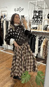 Pollera midi de corte amplio con estampado escocés en tonos marrones. Presenta un diseño distintivo con un sistema de cierre y ajuste en la cintura que simula puños de camisa anudados.