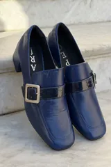 Mocasín de cuero vacuno color bordó con acabado charolado, punta cuadrada, taco bloque bajo y detalle de tira con hebilla metálica plateada en el empeine.
